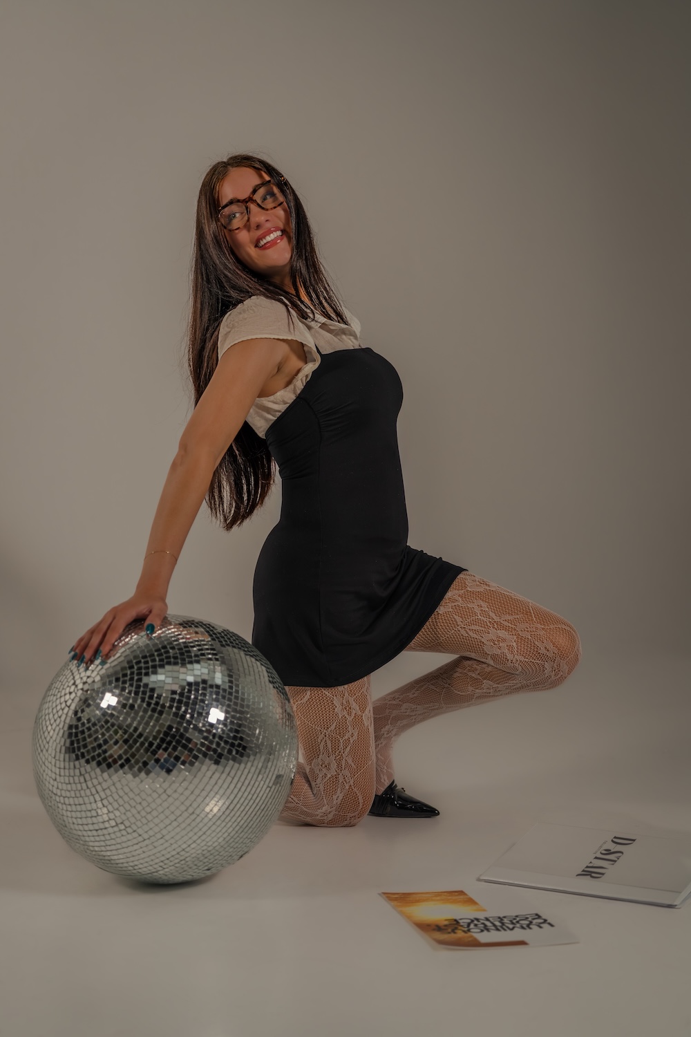 Delaney Starling leaning on a disco ball, smiling in a plain background studio.