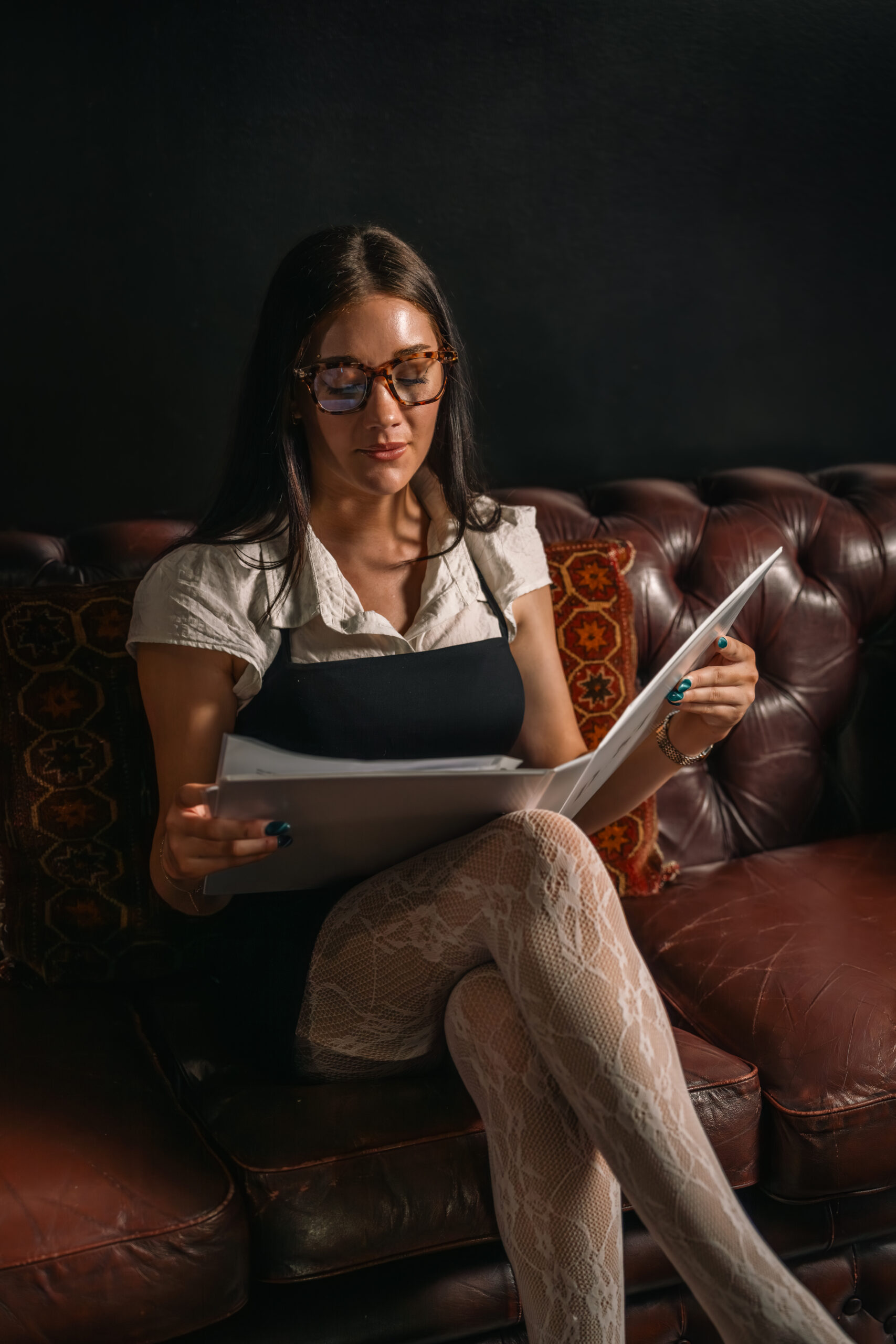 Delaney Starling sitting with portfolio binder in hand reading it. Dimly lit boudoir style photo